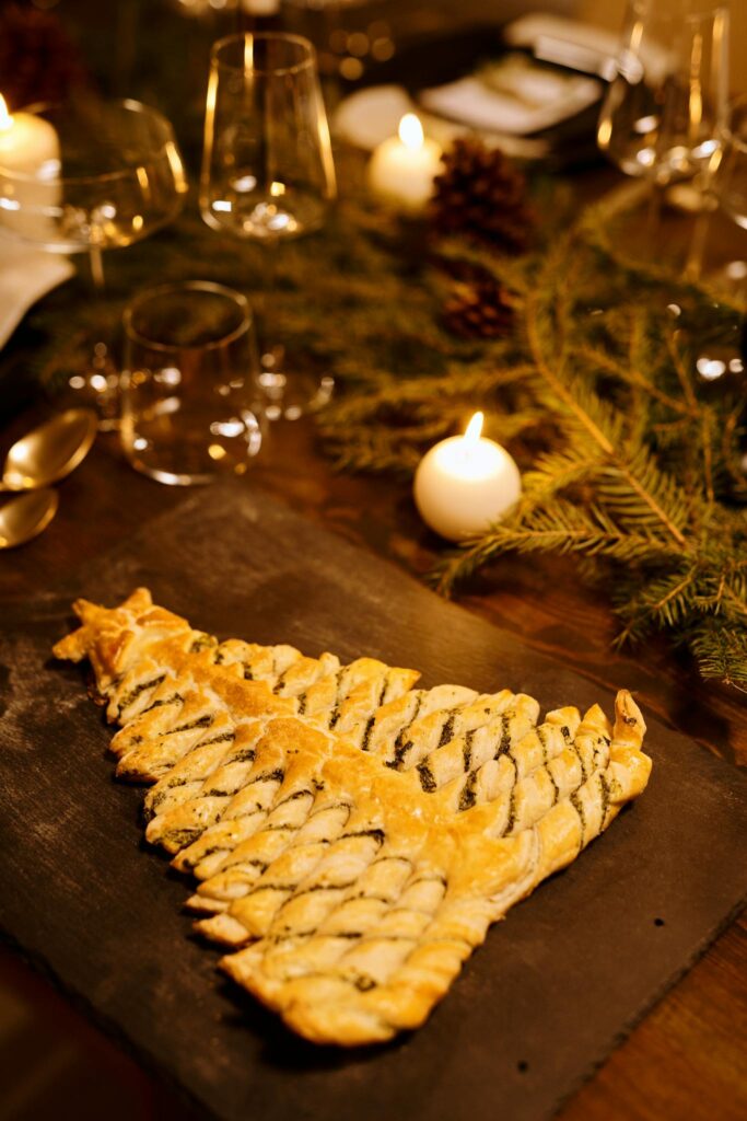 A beautifully baked Christmas tree-shaped pastry on a festive holiday dining table setting with candles.