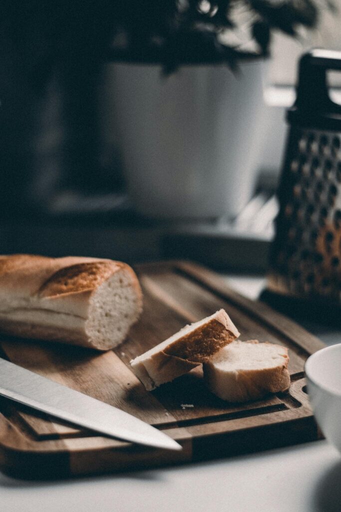 A sliced baguette with a knife on a wooden cutting board, in a cozy kitchen setting.