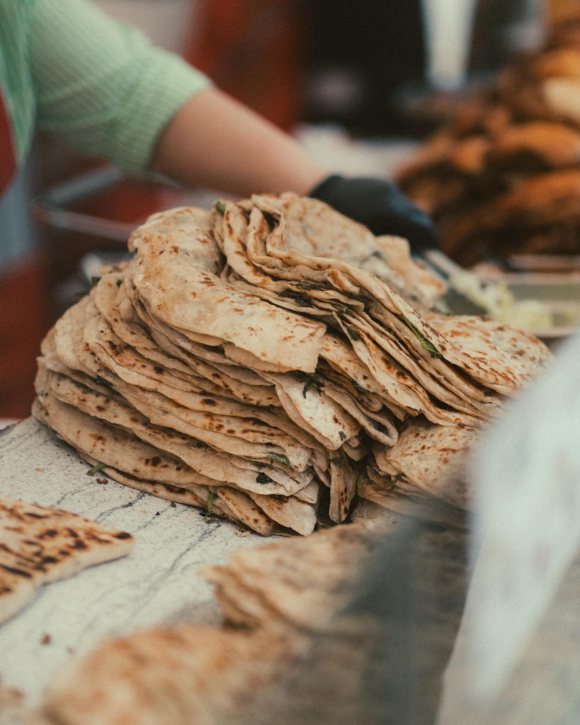 A stack of freshly cooked flatbreads at an outdoor market, ready for sale.