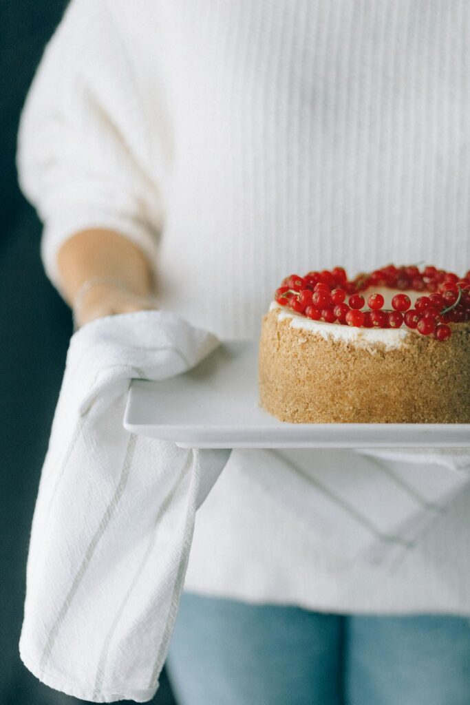 Woman holding a homemade cake decorated with red berries indoors. Cozy winter vibe.